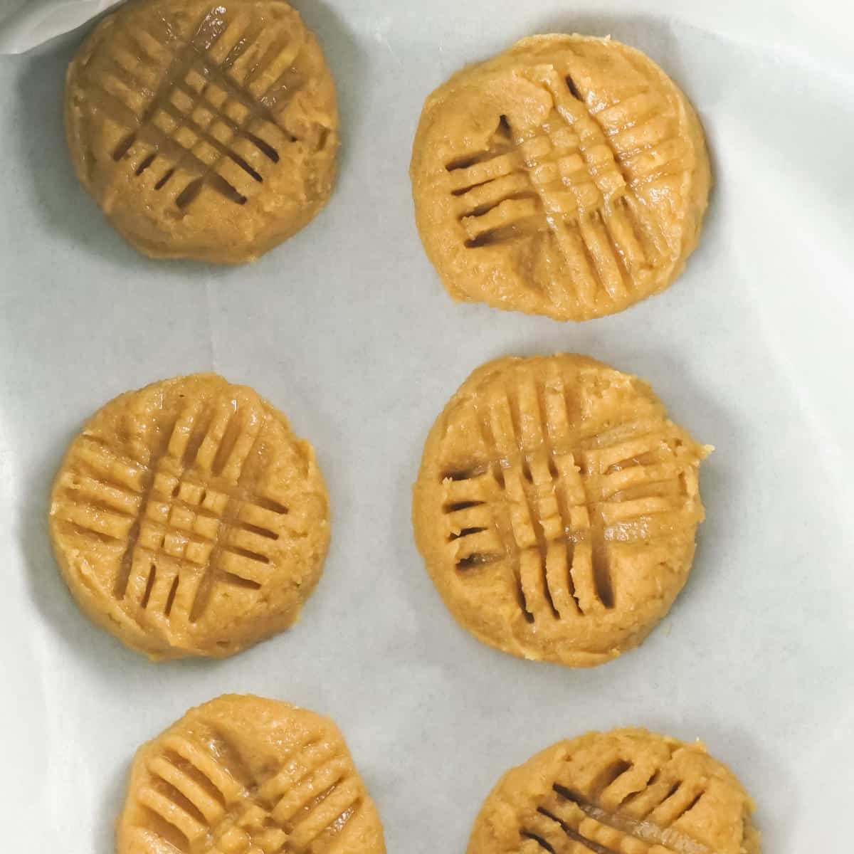 Peanut butter cookie balls smashed with fork tines on parchment paper.