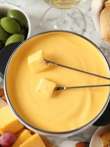 Pot of tasty cheese fondue, snacks and wine on white marble