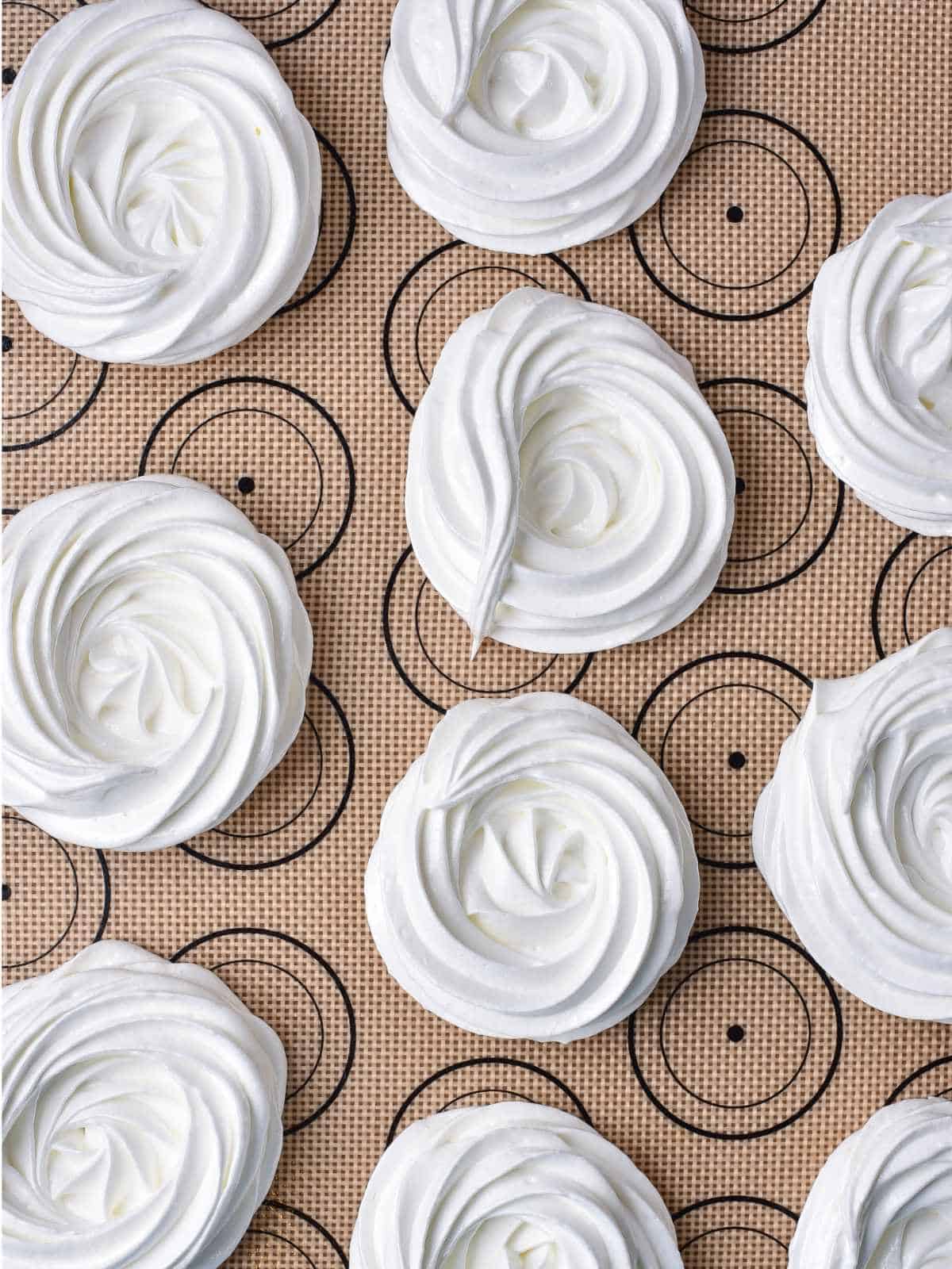 Swirled circles of whipped egg whites on baking mat.