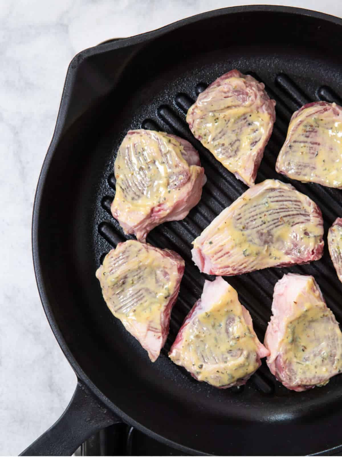 lamb chops coated in mustard in cast iron skillet.