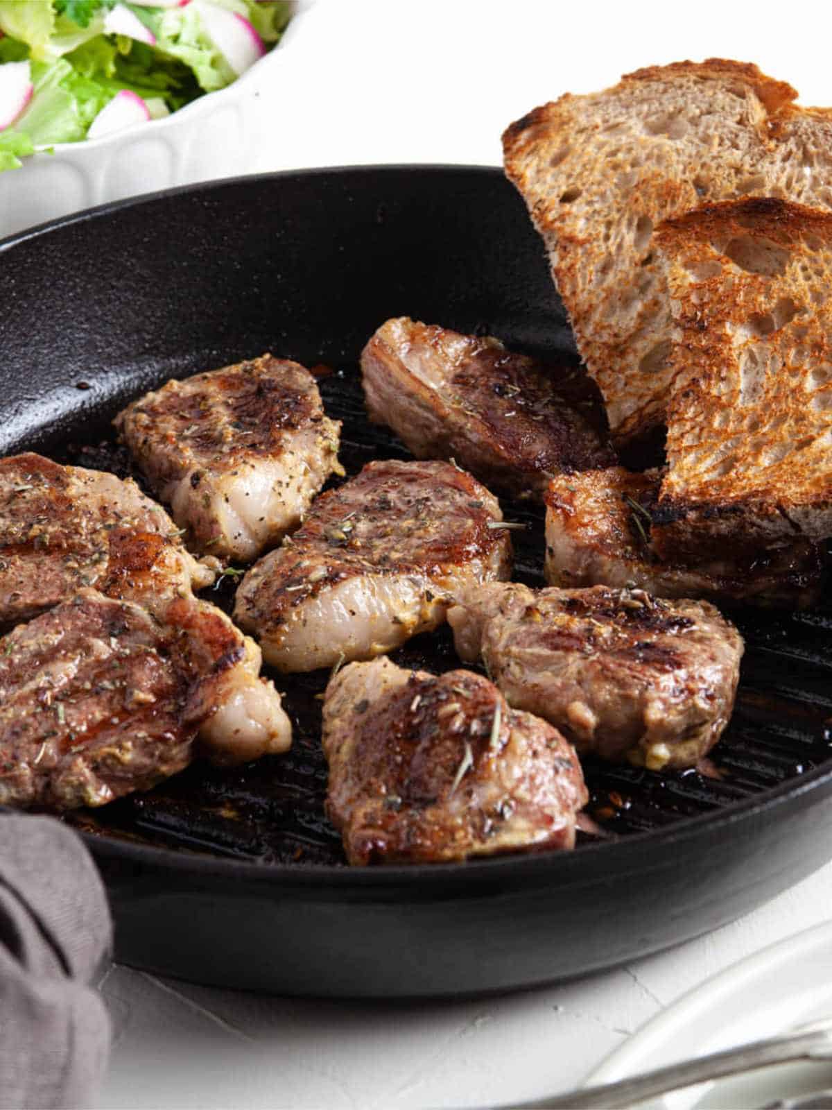 Pan seared lamb chops served in a cast iron skillet.