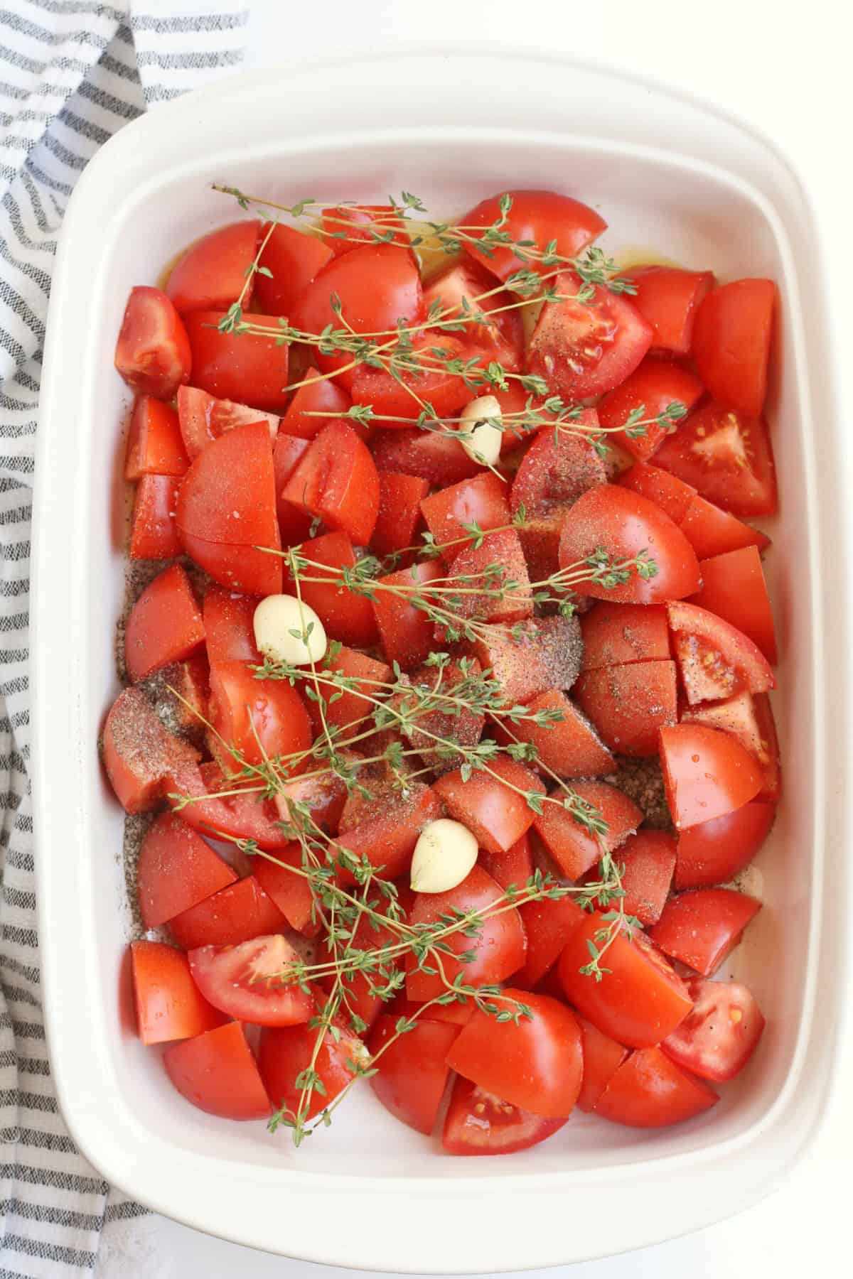 Tomatoes in a roasting pan with herbs and garlic cloves.