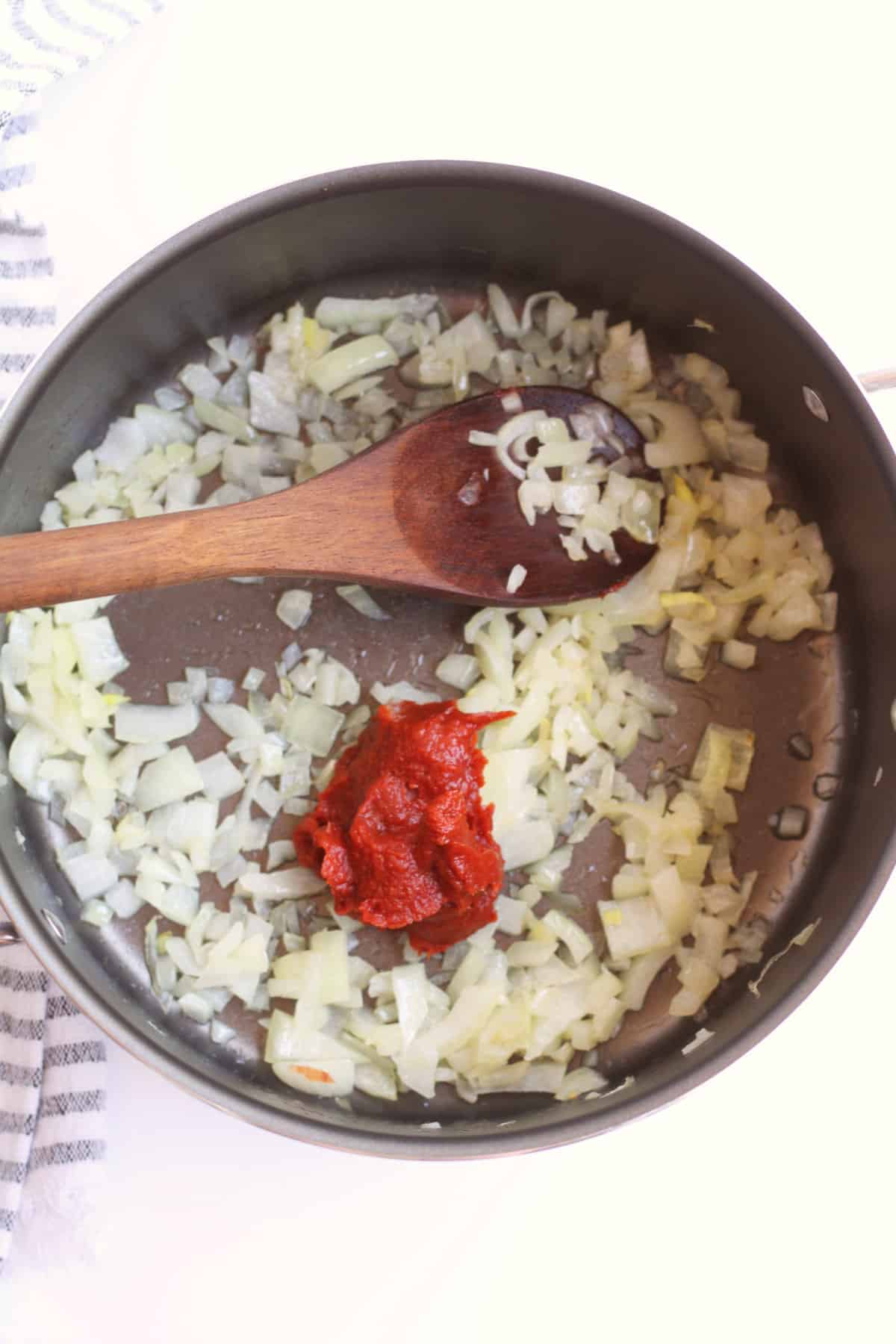 Soup pot with sauteed diced onions and a spoonful of tomato paste.
