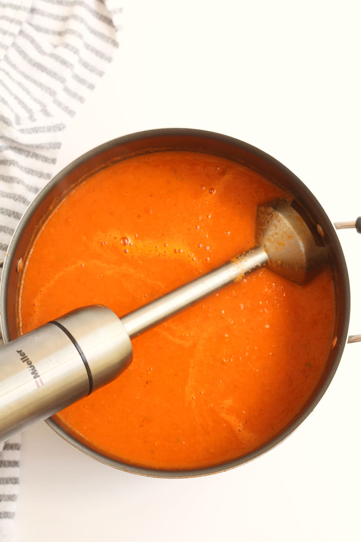 Pot of tomato soup being creamed smooth with an immersion blender.