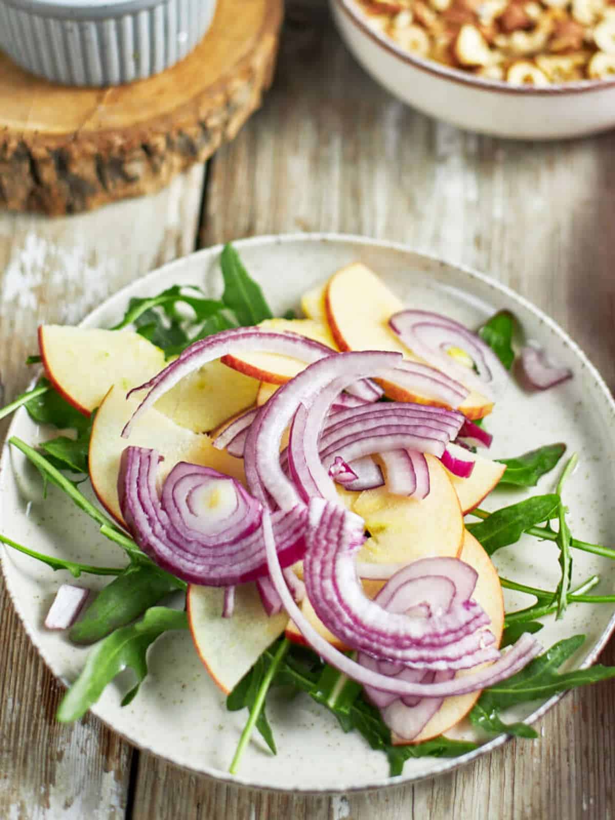 Sliced red onions on a plate with arugula and apple slices.
