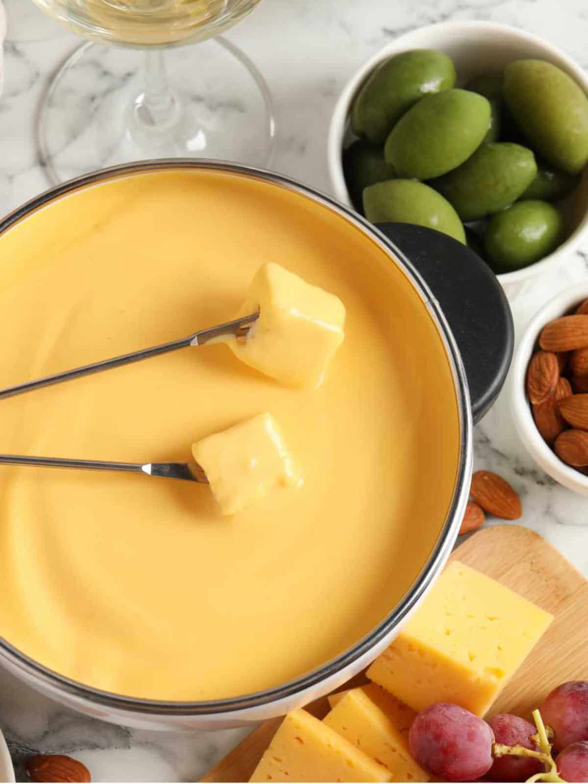 Pot of tasty cheese fondue, snacks and wine on white marble table.