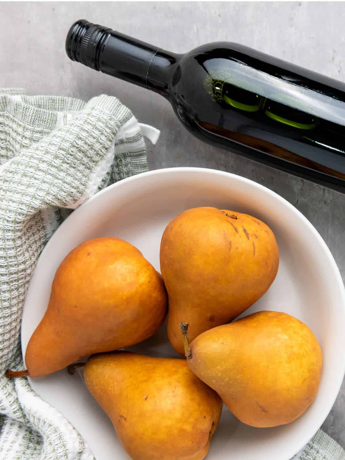 fresh golden pears in a bowl with a bottle of wine nearby.