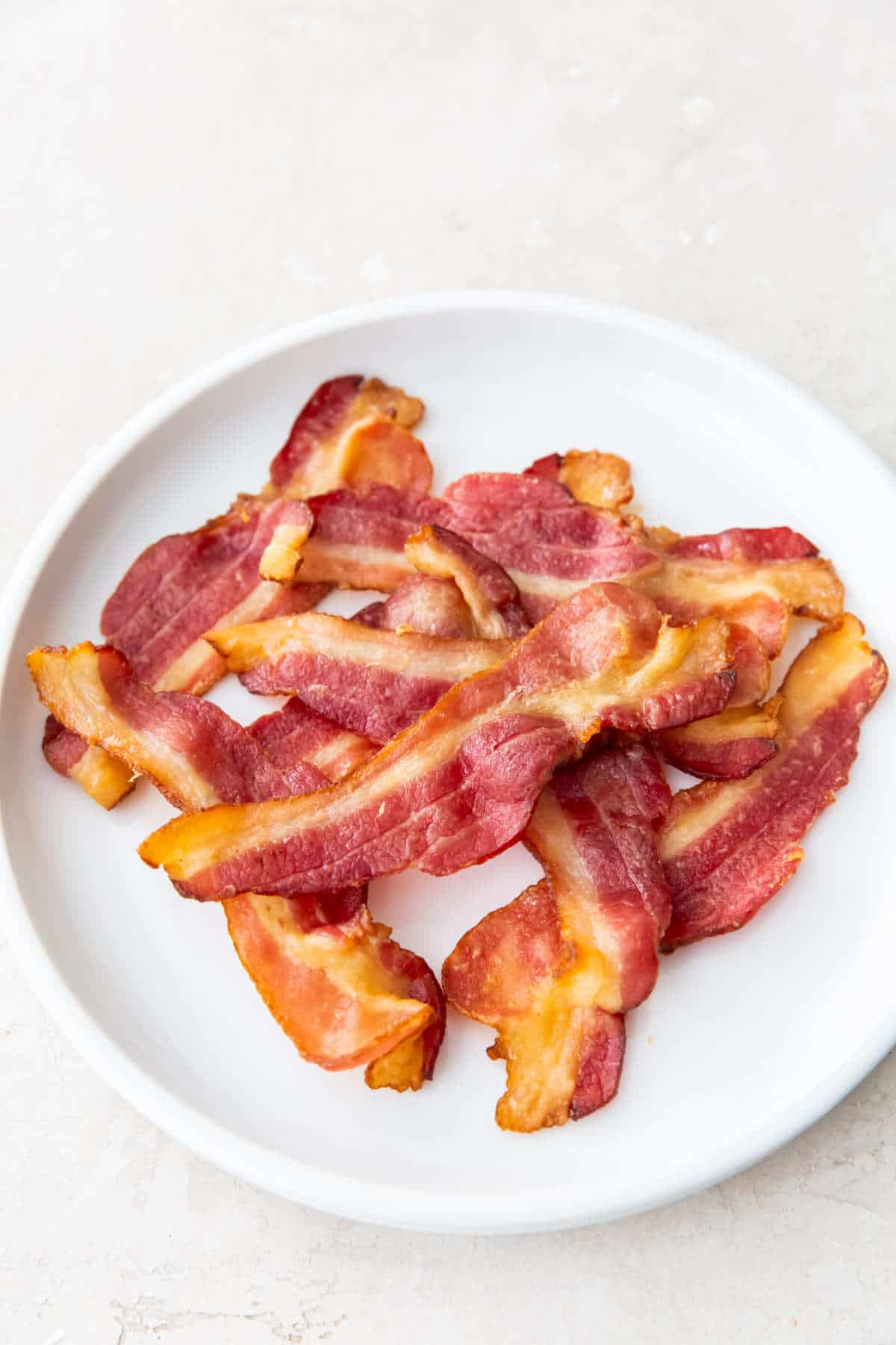 cooked crisp bacon cooling on a plate.